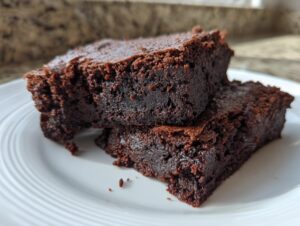 Two rich, dark chocolate date brownies stacked on a white plate, showing a dense, fudgy interior.