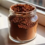 Close-up of rich brown homemade hot cocoa mix stored in a clear glass jar.