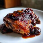 Close-up of a perfectly glazed braised chicken thighs piece covered in a rich, dark, fruity sauce.