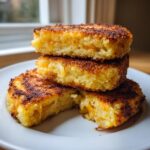 A stack of three golden brown, crispy mashed potato cakes, one cut open showing melted cheese inside.