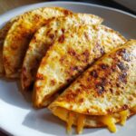Four golden brown, pan-fried cheesy pocket tacos lined up on a white plate, with melted cheese oozing out.