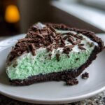 A close-up of a slice of no-bake grasshopper pie showing mint green filling, chocolate crust, and chocolate shavings.