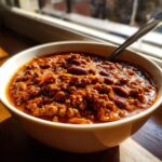 Close-up of a white bowl filled with rich, meaty chili, featuring kidney beans, ready to eat.