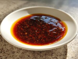 Glossy, dark brown homemade teriyaki sauce with visible specks, served in a small white dipping bowl.