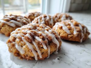 A close-up of several soft coffee cake cookies topped with cinnamon streusel and a white vanilla glaze drizzle.