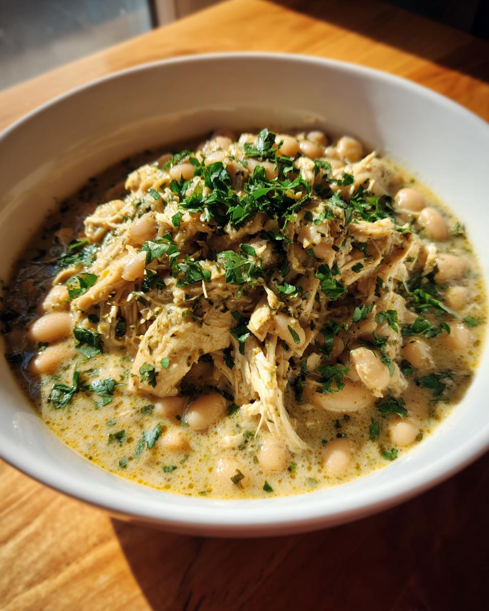 A close-up of a white bowl filled with creamy instant pot white chicken chili, topped with shredded chicken and fresh parsley.