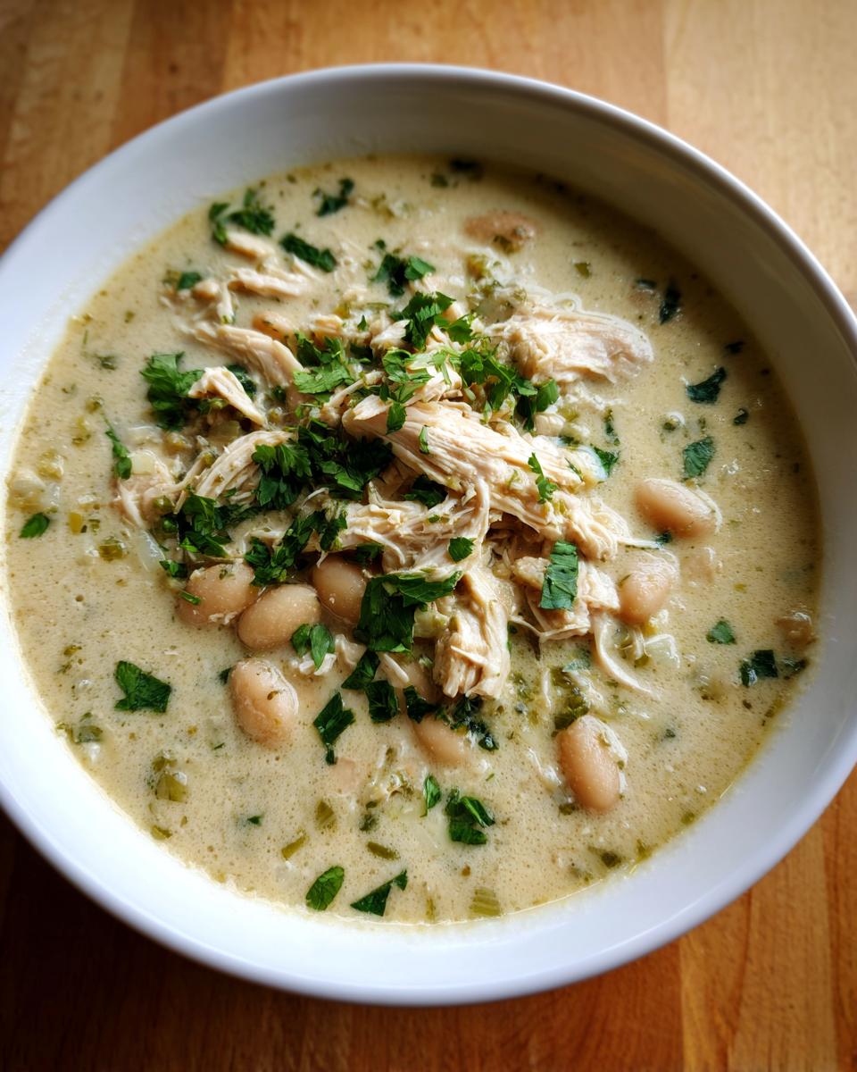 A close-up of a white bowl filled with creamy instant pot white chicken chili, topped with shredded chicken, white beans, and fresh parsley.