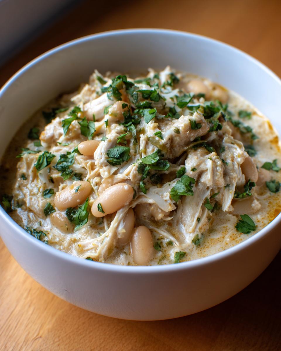 Close-up of a white bowl filled with creamy instant pot white chicken chili, shredded chicken, white beans, and fresh parsley.