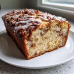 A freshly baked loaf of moist apple bread with a cinnamon swirl and white icing drizzled on top.