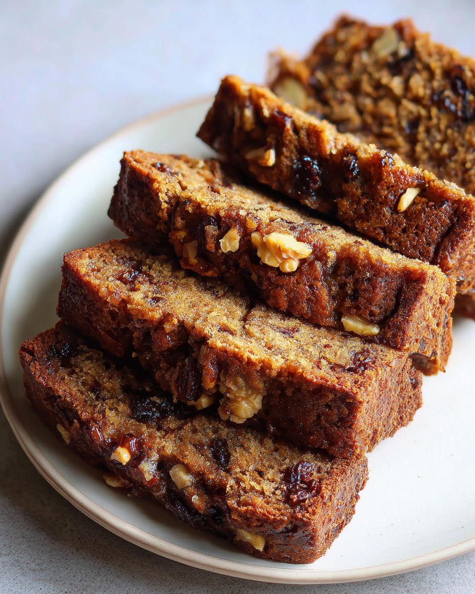 Close-up of four moist slices of date nut bread stacked on a white plate, showing visible walnuts and dates.