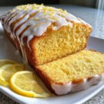 Close-up of a moist lemon loaf, sliced, drizzled with white glaze and topped with lemon zest.