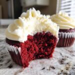 Close-up of a red velvet cupcakes with a bite taken out, showing the moist crumb and thick cream cheese frosting.