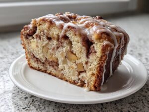 A thick slice of moist apple bread with visible apple chunks and cinnamon swirl, topped with a sweet vanilla glaze.