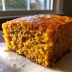 Close-up of a square slice of moist, orange sweet potato cornbread topped with a shiny glaze.