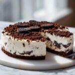 A creamy, no-bake Oreo cheesecake topped with cookie crumbs and whole cookies, with one slice cut out.