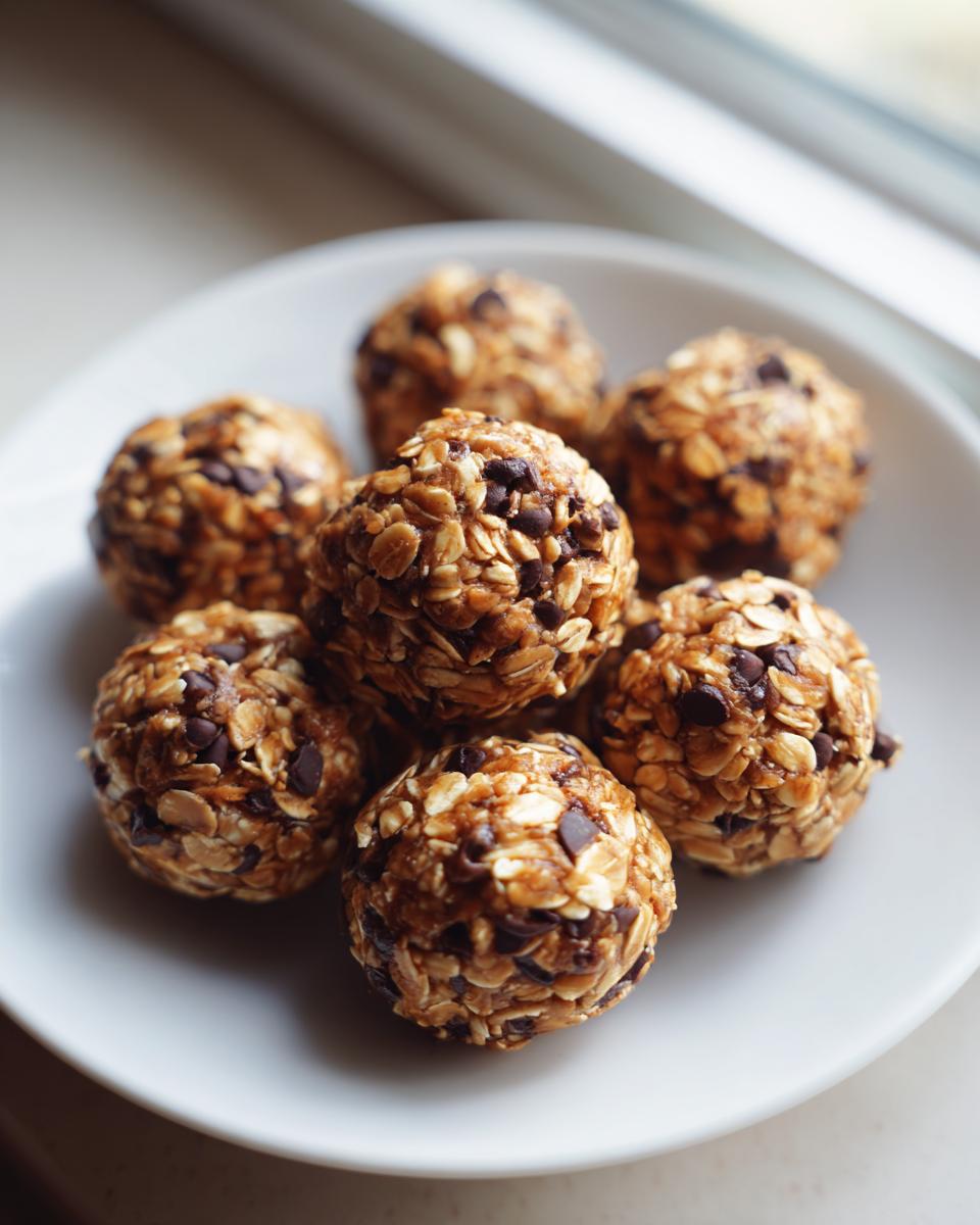 A small white plate holds several homemade protein balls coated in oats and mini chocolate chips.