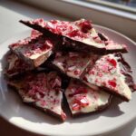 A pile of broken pieces of dark and white chocolate peppermint bark recipe topped with crushed candy canes.