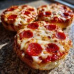 Three freshly baked pepperoni english muffin pizza snacks topped with melted cheese and herbs.