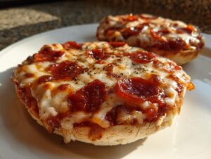 Two freshly baked pepperoni english muffin pizza halves topped with melted cheese and herbs on a white plate.