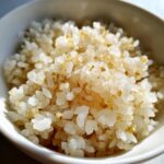 Close-up of glistening, perfectly cooked sushi rice grains with a slight golden sheen in a white bowl.