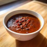 Close-up of a hearty bowl of rich, dark red black bean soup with visible whole beans and diced tomatoes.
