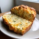 A close-up of savory soda bread, sliced to show cheese and herbs baked inside.