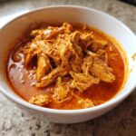 Close-up of shredded chicken coated in a vibrant orange-red sauce, ready for slow cooker buffalo chicken chili.