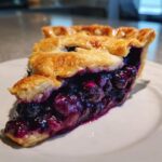 Close-up of a thick slice of homemade blueberry pie recipe showing juicy filling and flaky crust.