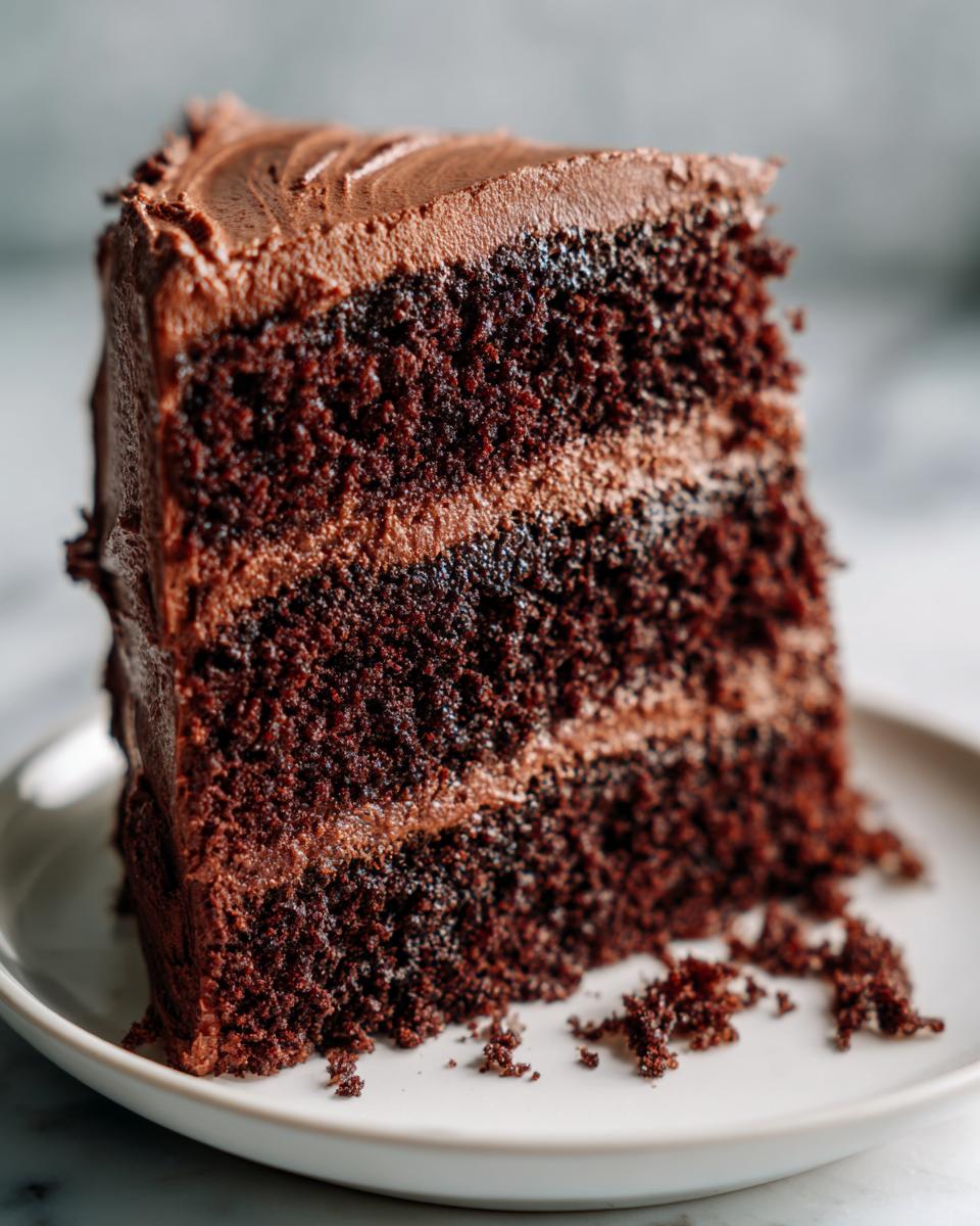 Close-up of a rich, dark slice of homemade chocolate cake with three layers and chocolate frosting.