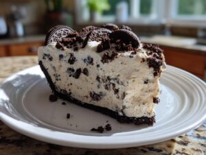 A generous slice of creamy, no-bake oreo pie with chunks of cookies in the filling, topped with crumbs and whole cookies.