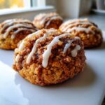 A close-up of a soft coffee cake cookie coated in cinnamon sugar and drizzled with white icing.