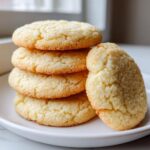 A stack of four soft sugar cookie rounds, with one leaning against the side, coated in sparkling sugar.
