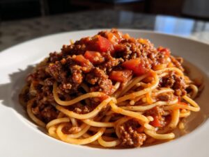 A close-up of spaghetti topped generously with rich, meaty bolognese sauce and chunks of tomato.