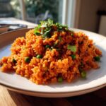 A mound of vibrant orange Spanish rice mixed with green peas and topped with fresh cilantro on a white plate.