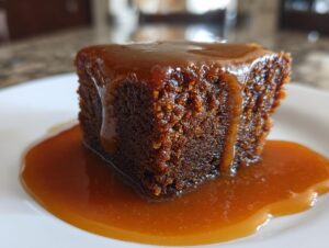 Close-up of a square slice of dark, moist sticky toffee pudding drenched in rich toffee sauce.