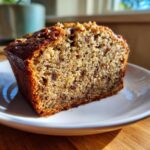 Close-up of a moist slice of sugar free banana bread with visible chocolate chips and walnuts on top.