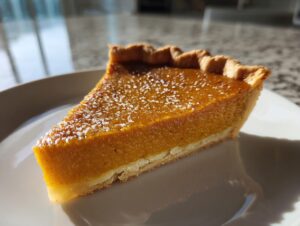 A close-up slice of amazing vegan pumpkin pie dusted with powdered sugar on a white plate.