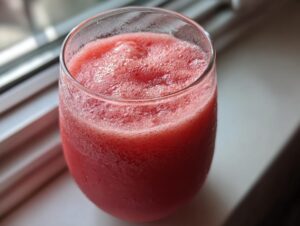 Close-up of a frosty glass filled with a vibrant red watermelon smoothie, sitting near a window.