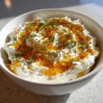 A white bowl filled with creamy whipped feta dip, drizzled generously with golden honey and garnished with fresh dill sprigs.