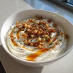 A close-up of creamy whipped ricotta dip topped with candied walnuts, honey drizzle, and fresh thyme.