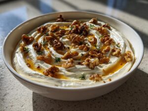A bowl of creamy whipped ricotta dip swirled and topped with candied walnuts, honey drizzle, and fresh thyme.