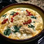 A close-up of a bowl of rich white chicken lasagna soup with shredded chicken, spinach, and sun-dried tomatoes.