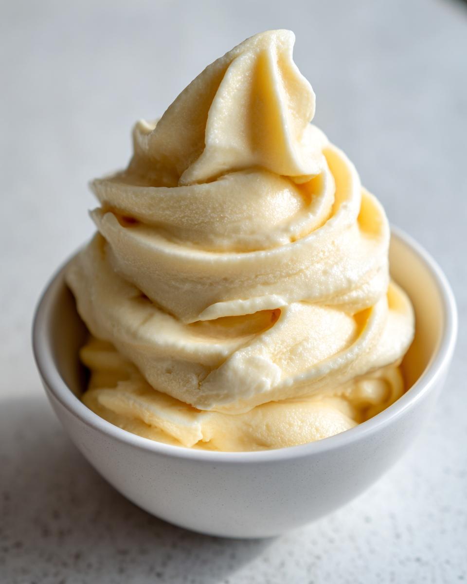Close-up of soft-serve style banana ice cream swirled high in a small white bowl.