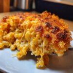 A close-up serving of creamy baked mac and cheese with a golden, crispy topping being lifted by a fork.