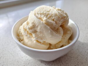 A close-up of creamy, pale yellow banana ice cream scooped into a small white bowl.