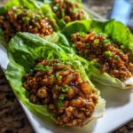 A close-up view of several servings of savory chicken lettuce wraps garnished with green onions on a white platter.