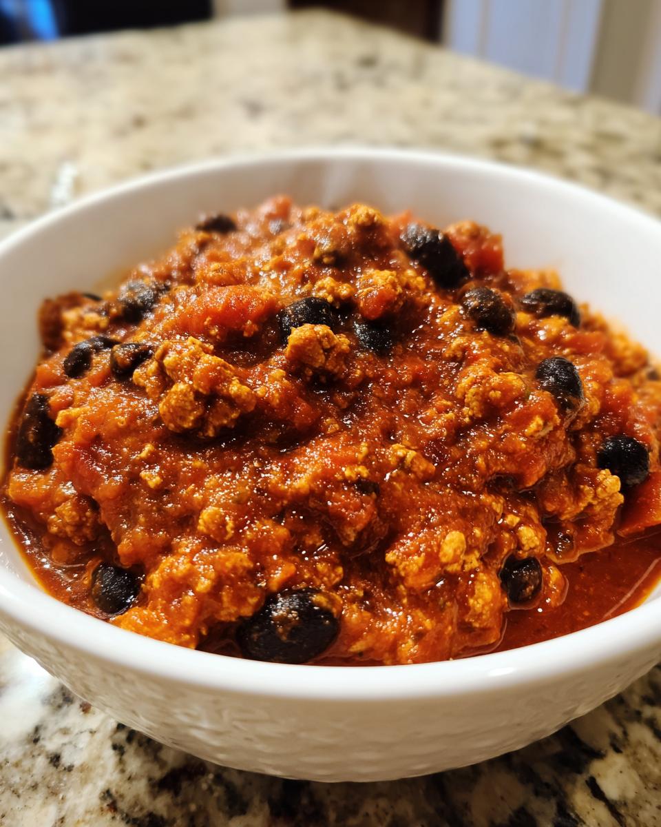 Close-up of a white bowl filled with rich, thick pumpkin chili featuring ground meat and black beans.