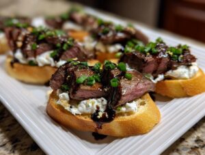 Close-up of several delicious steak crostini appetizers topped with rare steak, creamy cheese, and green onions.
