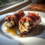 Close-up of two bacon wrapped stuffed dates, oozing with creamy filling and drizzled with honey.