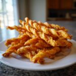 A pile of golden brown, twisted cheese straws recipe snacks stacked high on a white plate.